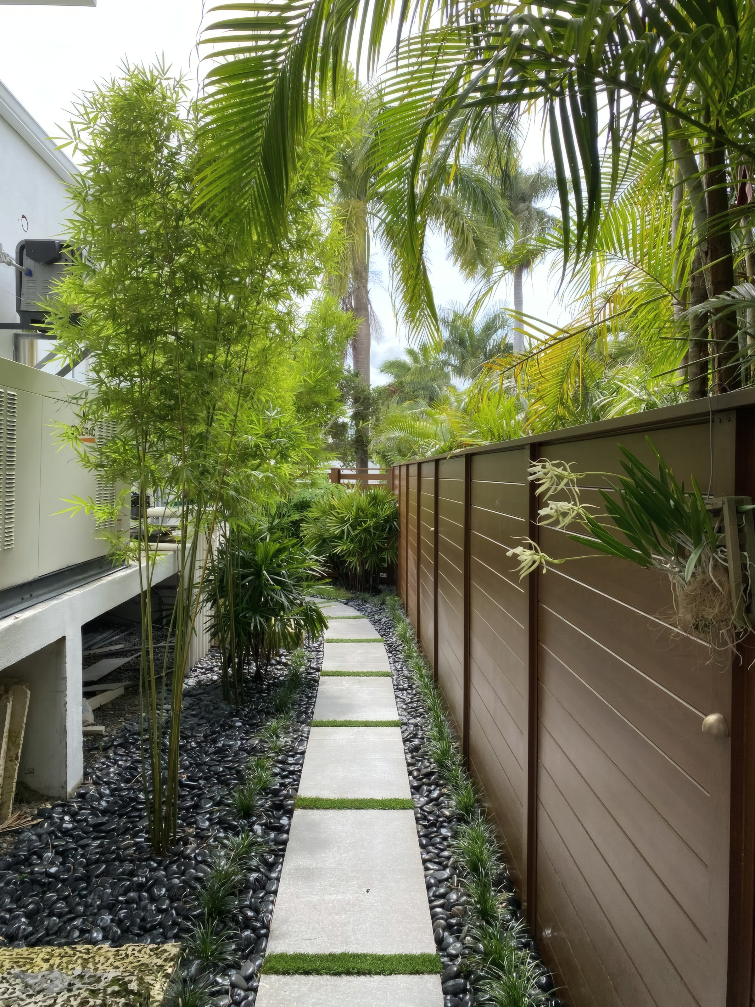 After: finished corridor with horizontal wood fence, bamboo, and a paver walkway
