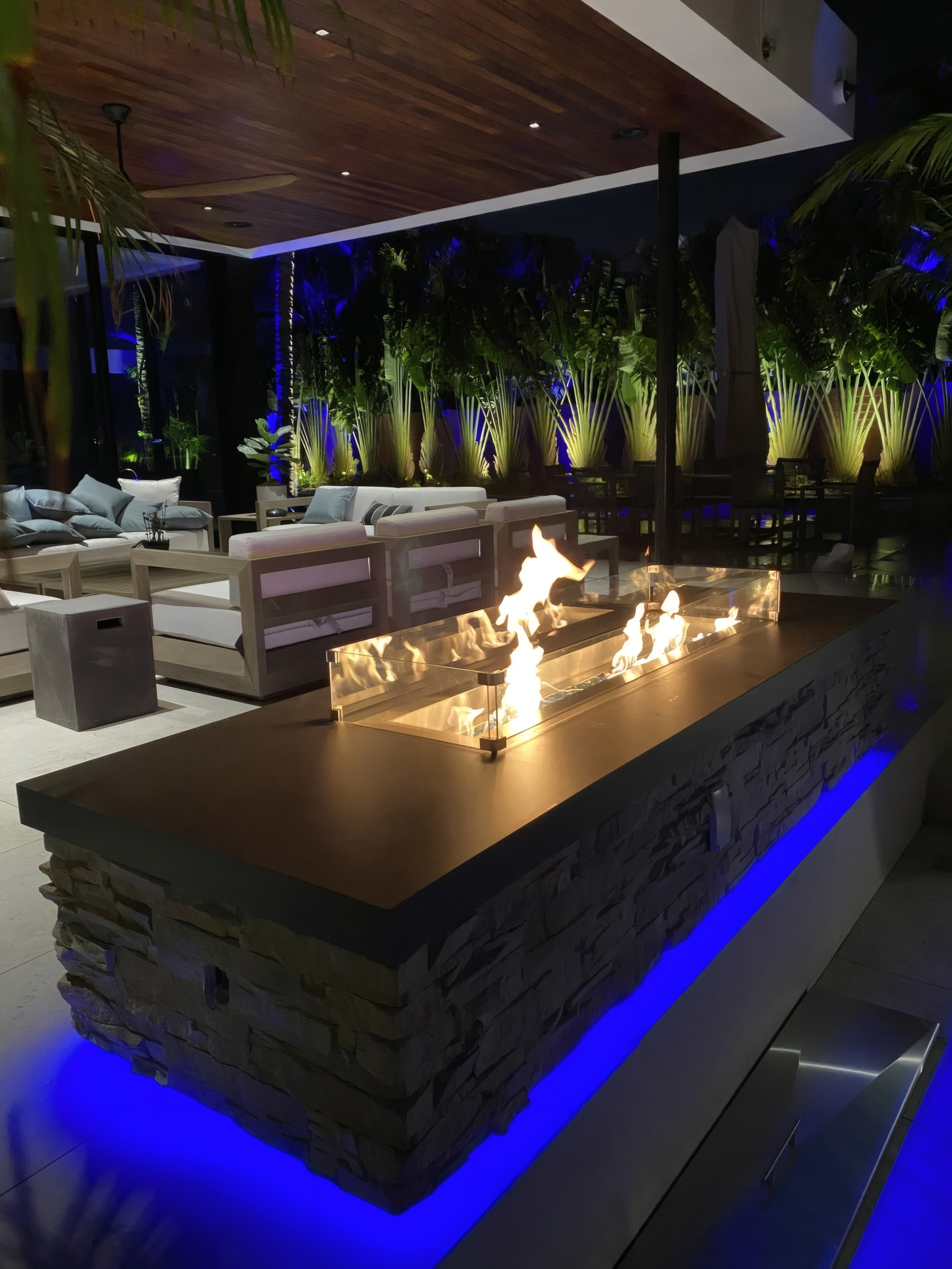 Long linear fire feature with sectionals and blue-uplit traveler palms